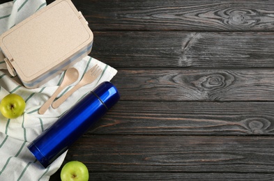 Thermos, lunch box and apples on black wooden table, flat lay. Space for text