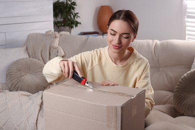 Young woman using utility knife to open parcel at home