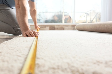 Photo of Man measuring carpet indoors. Construction tool