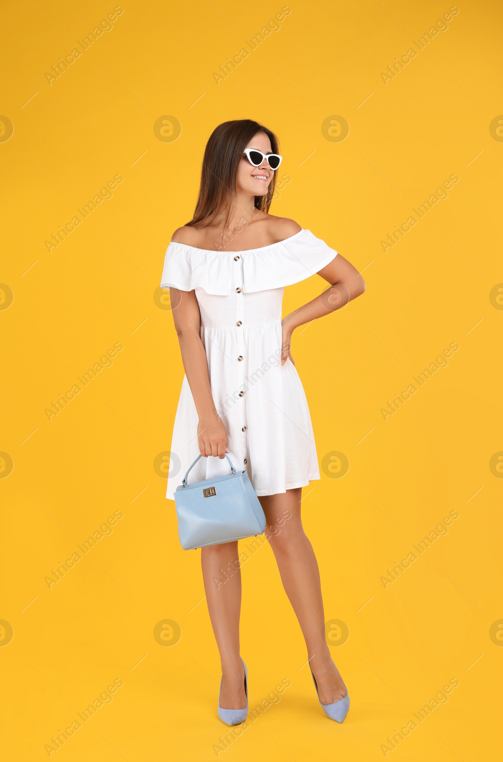 Photo of Young woman wearing stylish white dress with elegant bag on yellow background