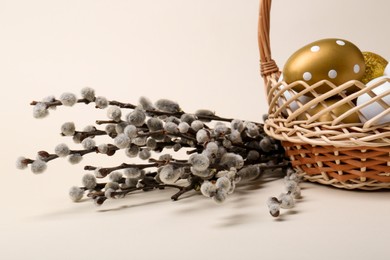 Photo of Wicker basket with decorated Easter eggs and willow branches on beige background, closeup
