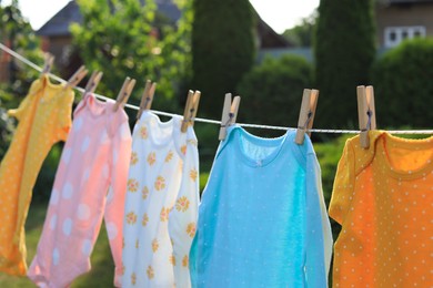Photo of Clean baby onesies hanging on washing line in garden. Drying clothes