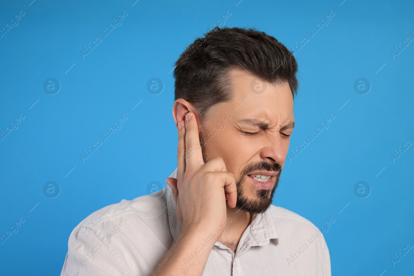 Photo of Man suffering from ear pain on light blue background