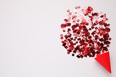 Shiny red confetti bursting out of party cracker on light background, top view. Space for text