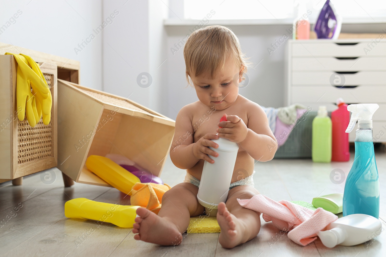 Photo of Cute baby playing with bottle of detergent on floor at home. Dangerous situation