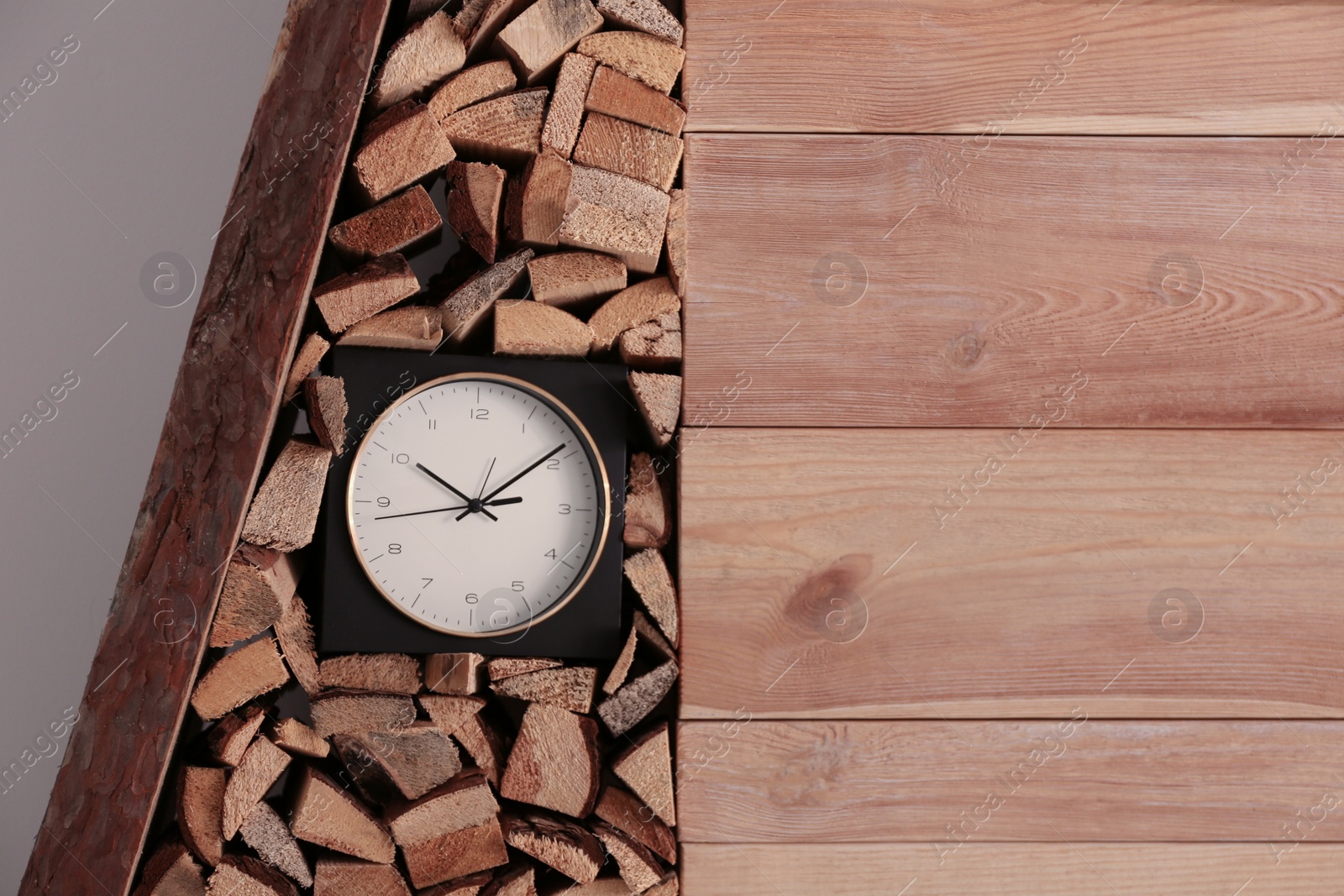 Photo of Clock and stacked firewood near wall indoors. Idea for interior design