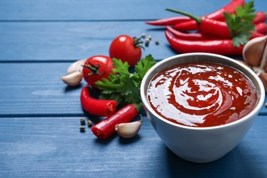 Photo of Spicy chili sauce in bowl on blue wooden table, space for text