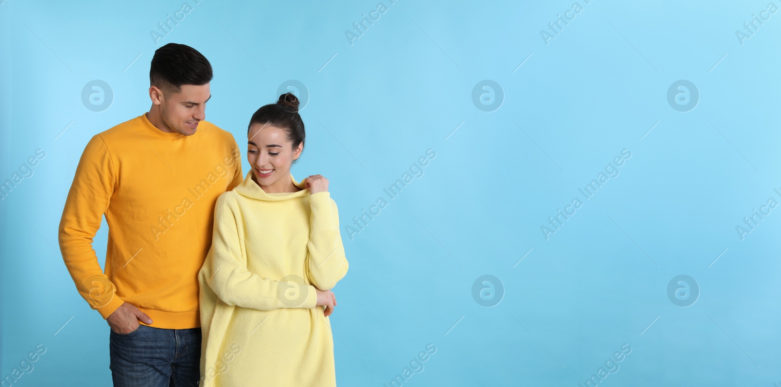 Photo of Happy couple wearing yellow warm sweaters on light blue background. Space for text