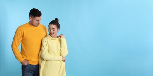 Happy couple wearing yellow warm sweaters on light blue background. Space for text