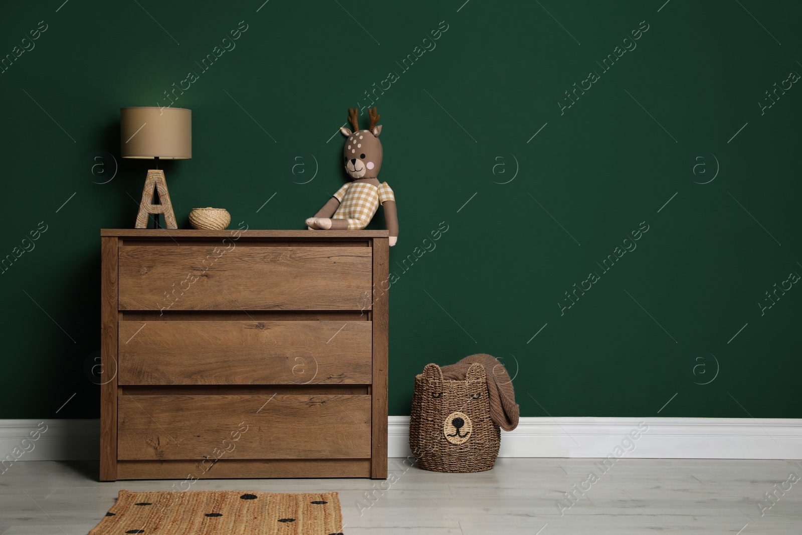 Photo of Modern wooden chest of drawers with lamp and toy near green wall indoors. Space for text