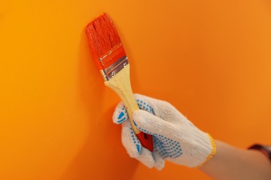 Photo of Designer painting orange wall with brush, closeup