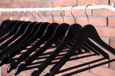 Photo of Black clothes hangers on rack near red brick wall, closeup