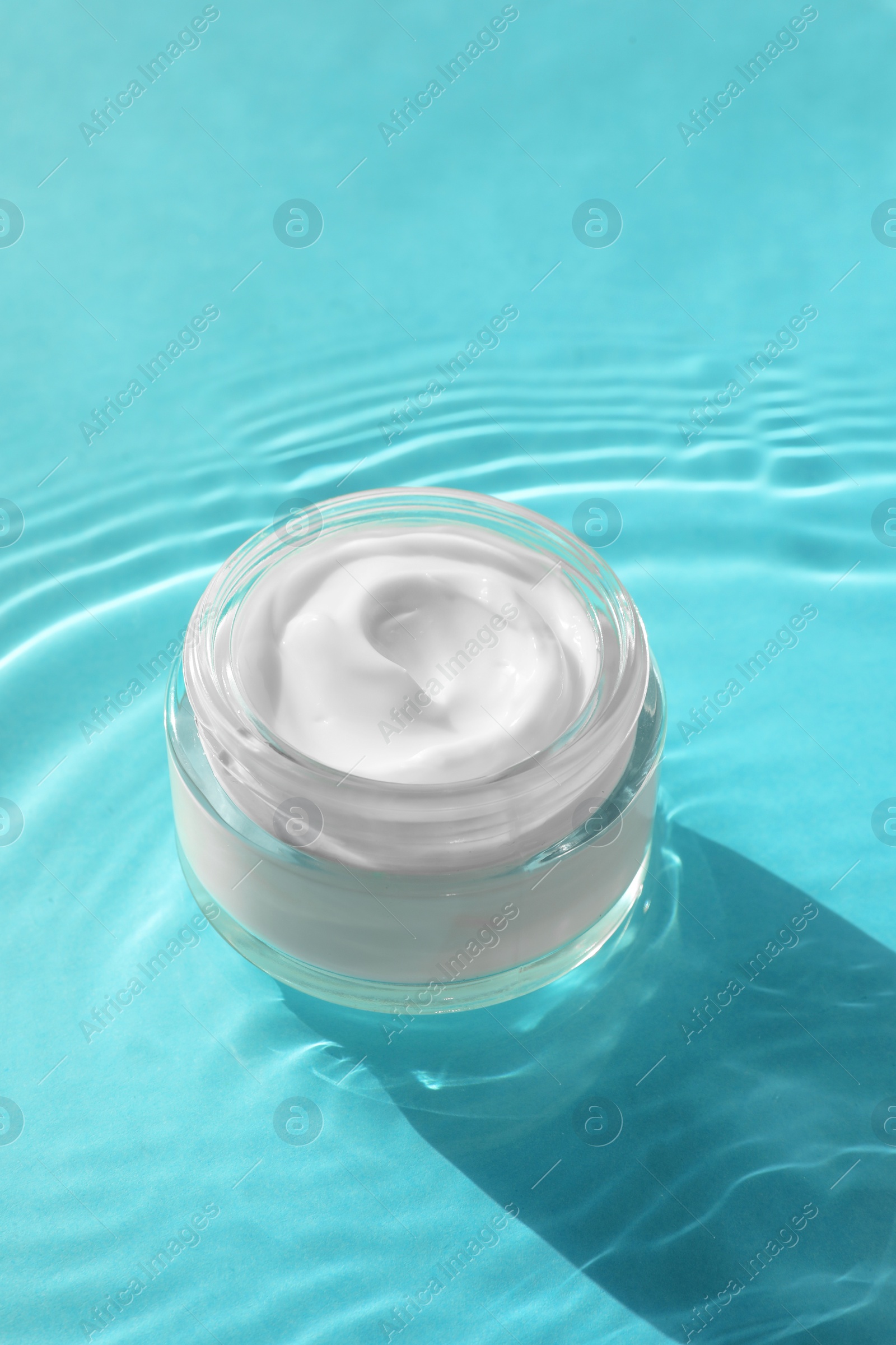 Photo of Jar with moisturizing cream in water on light blue background