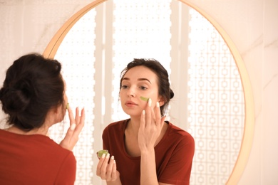 Young woman applying mask on her face near mirror in bathroom