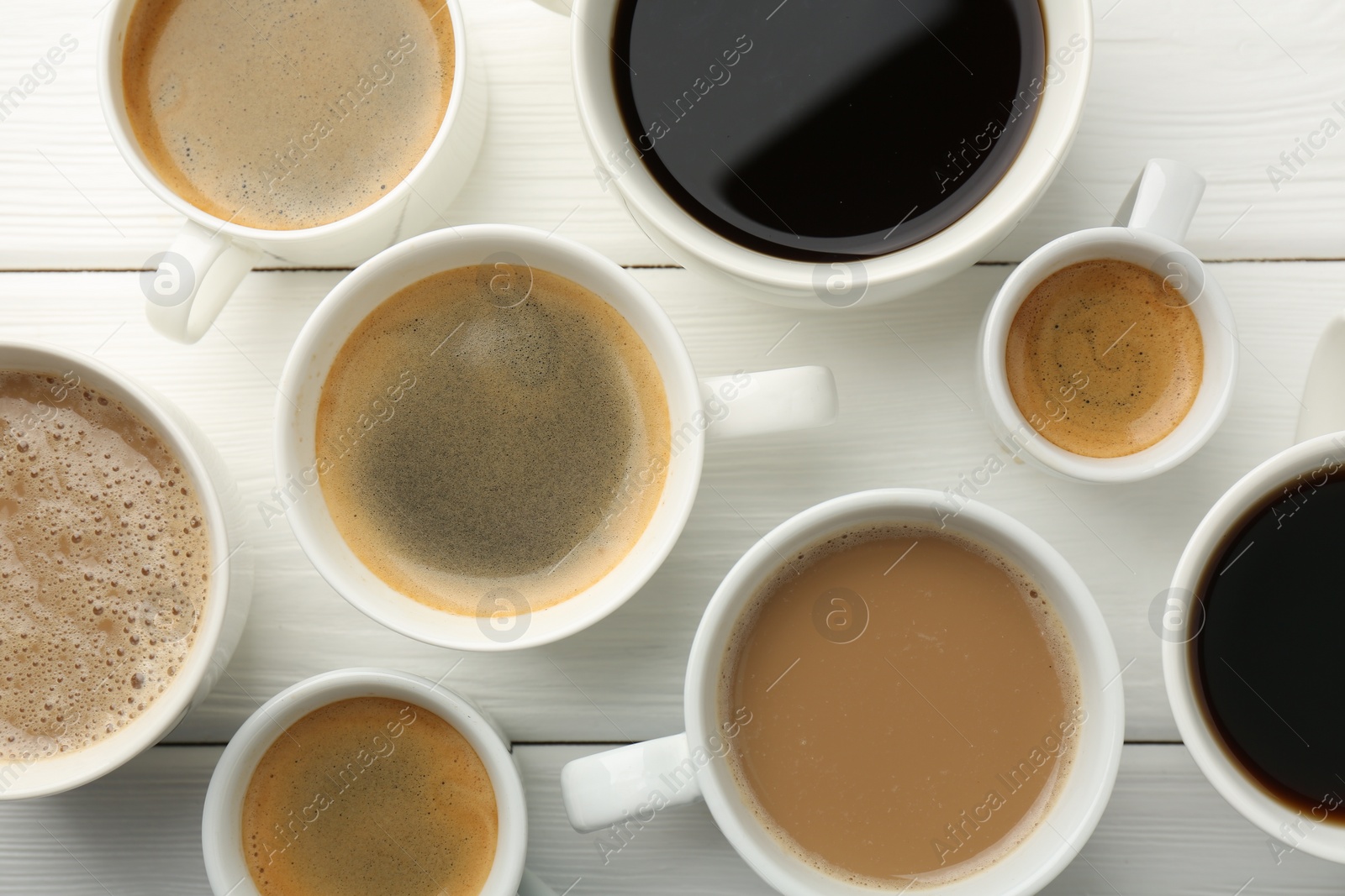 Photo of Different coffee drinks in cups on white wooden table, flat lay