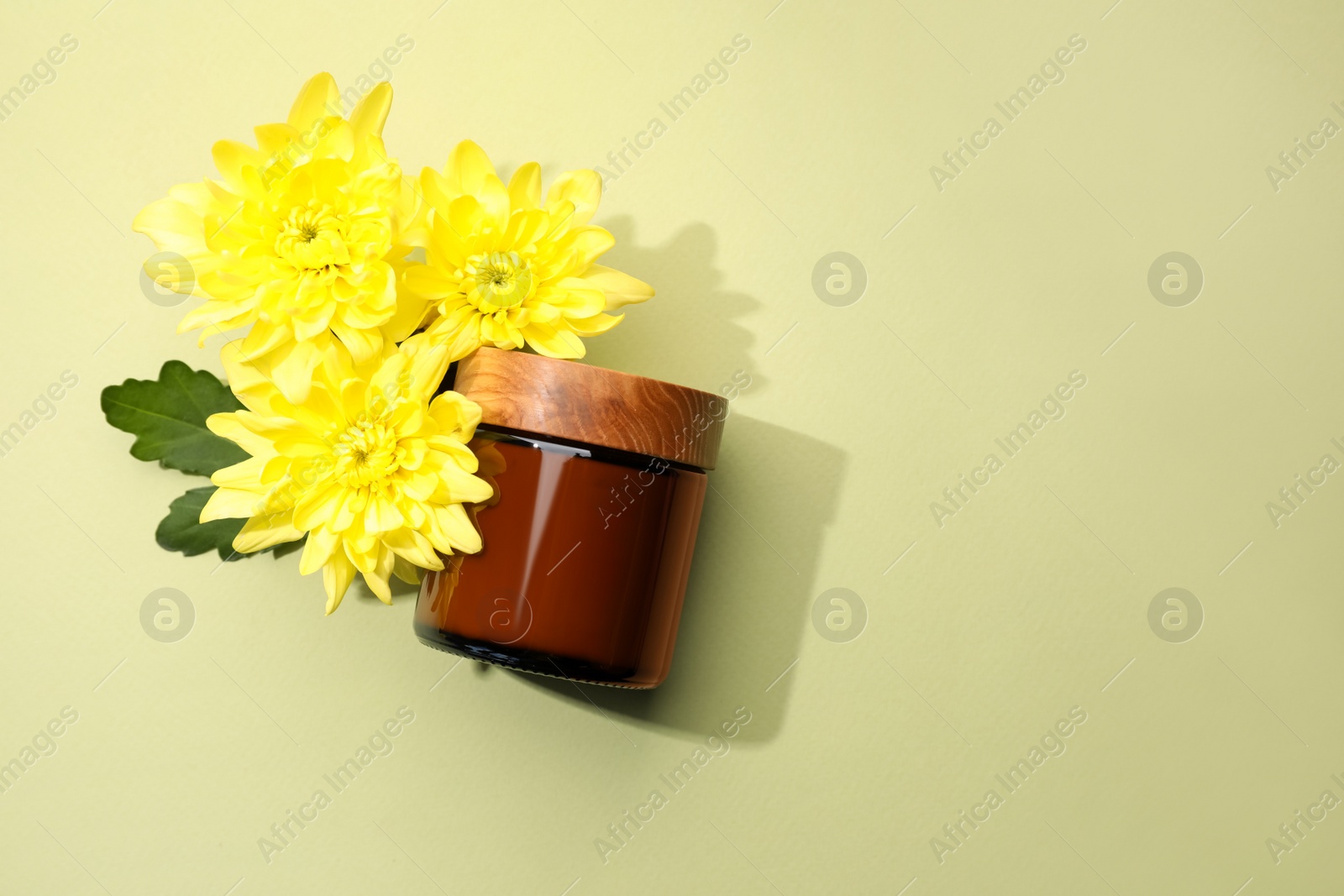 Photo of Glass jar of face cream and flowers on pale olive background, flat lay. Space for text