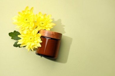 Photo of Glass jar of face cream and flowers on pale olive background, flat lay. Space for text