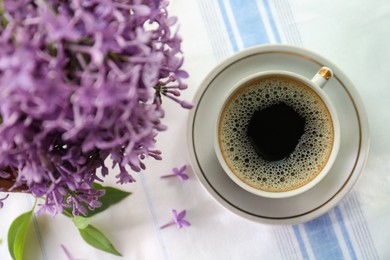 Photo of Beautiful lilac flowers and cup of hot coffee on fabric, flat lay