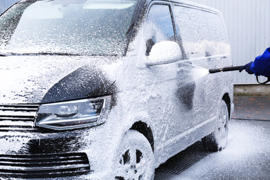 Photo of Worker covering automobile with foam at car wash, closeup