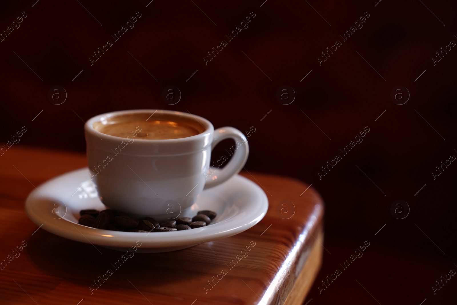 Photo of Cup of hot aromatic coffee and roasted beans on wooden table in cafe. Space for text