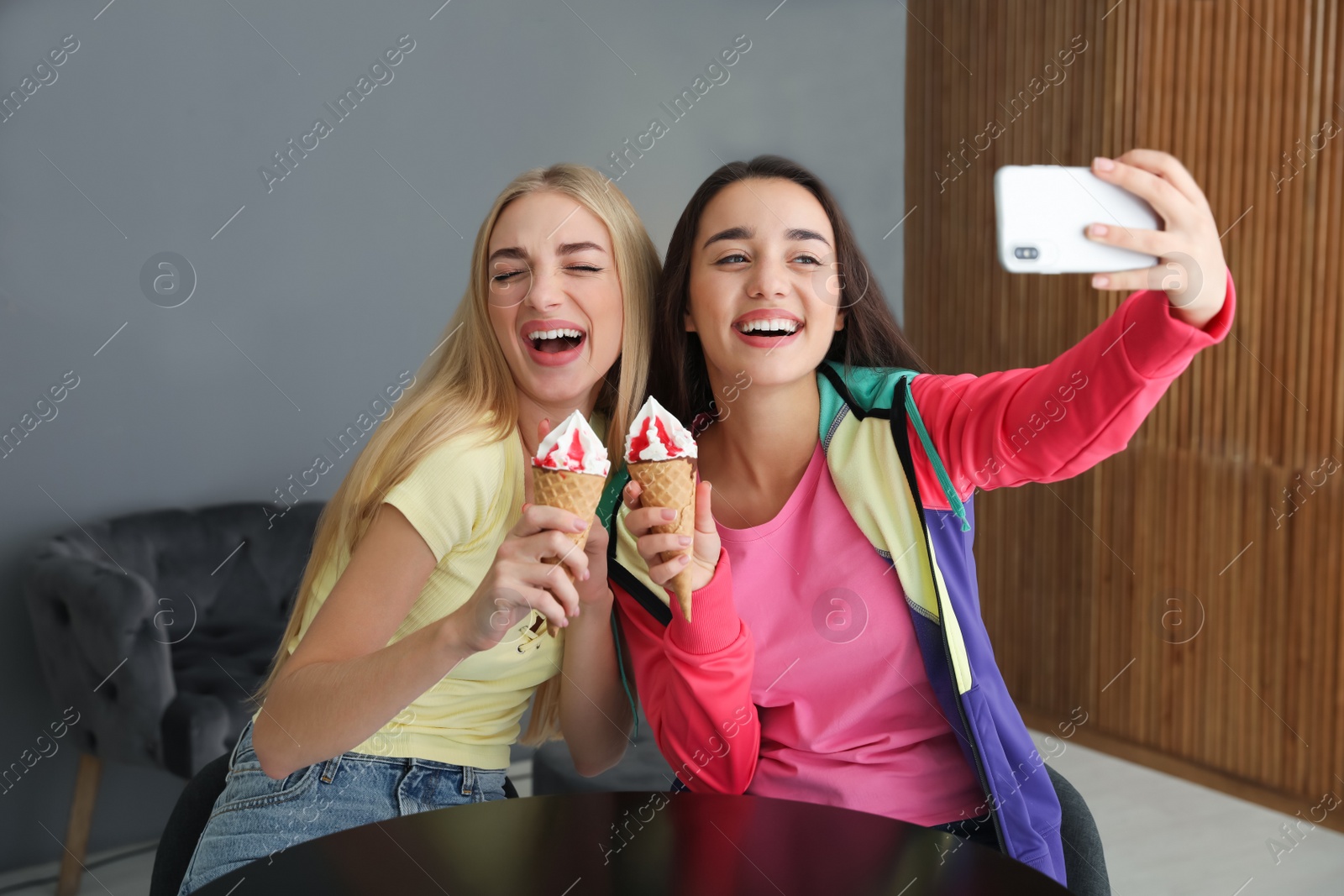 Photo of Young women with ice cream laughing while taking selfie indoors