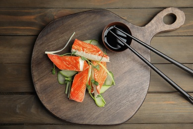 Fresh crab sticks with cucumber and soy sauce served on wooden table, flat lay