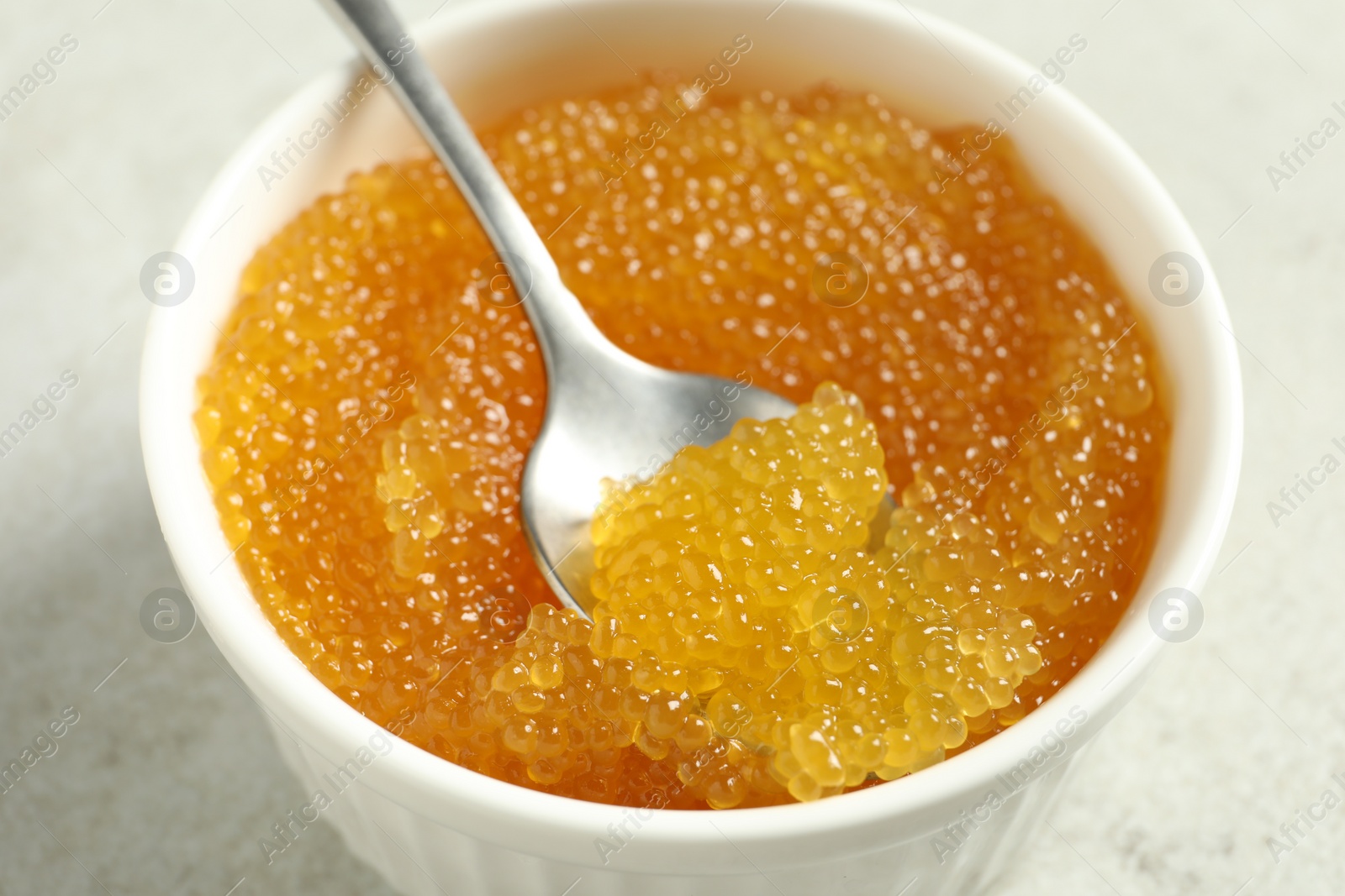 Photo of Fresh pike caviar in bowl and spoon on light grey table, closeup