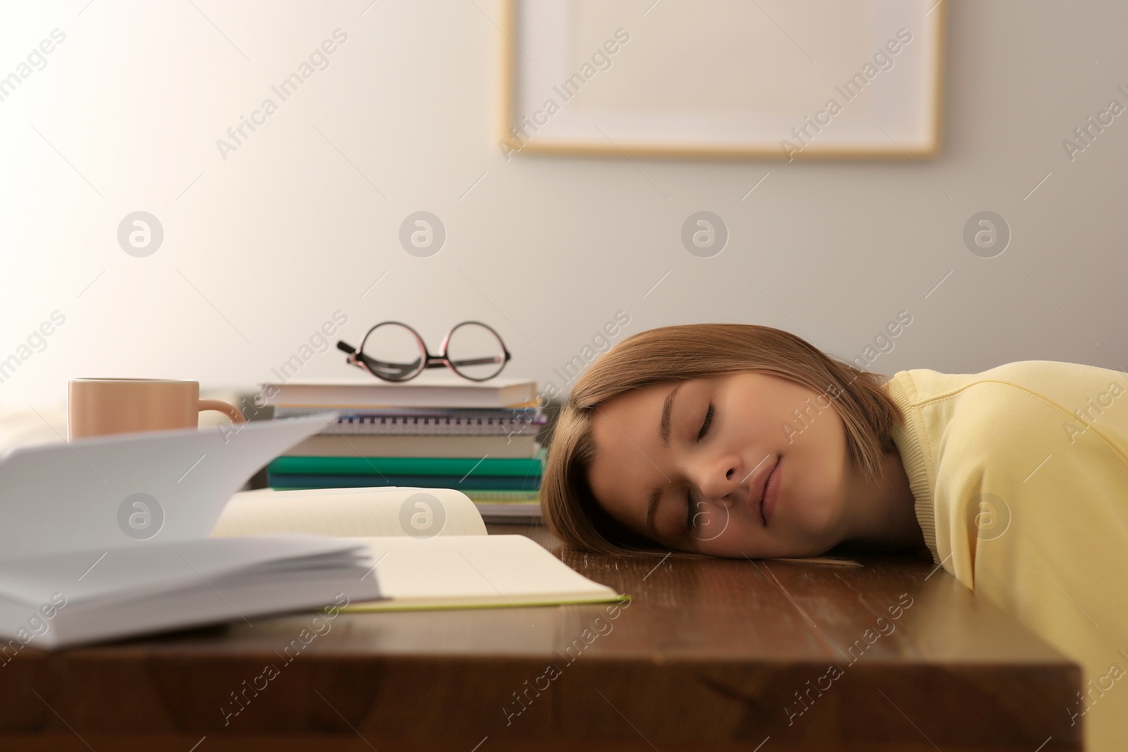 Photo of Young tired woman sleeping near books at wooden table indoors