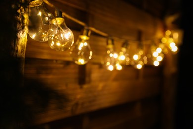 Photo of Garland of lamp bulbs hanging on wooden wall, space for text. String lights