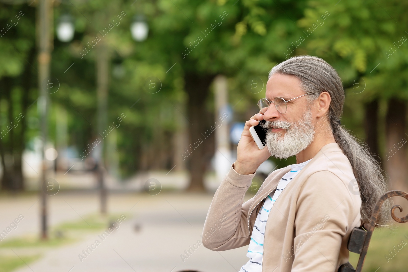 Photo of Handsome mature man with mobile phone sitting on bench in green park