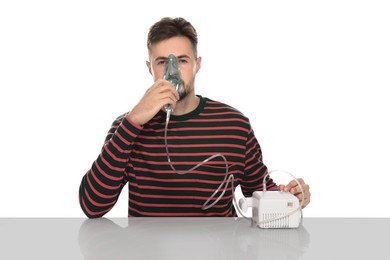 Photo of Man using nebulizer for inhalation at table on white background