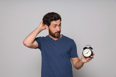 Emotional bearded man with alarm clock on light grey background. Being late concept