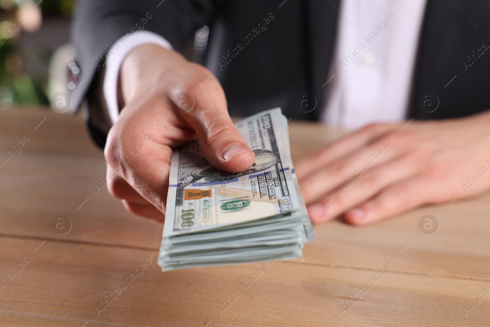 Photo of Money exchange. Man holding dollar banknotes at wooden table, closeup