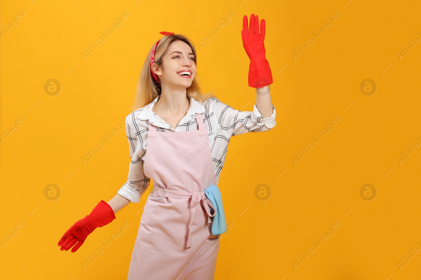 Photo of Young housewife in gloves on yellow background. Space for text