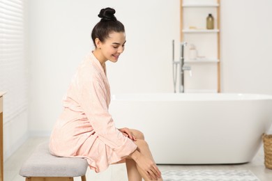 Photo of Beautiful happy woman in stylish bathrobe sitting on bench in bathroom. Space for text
