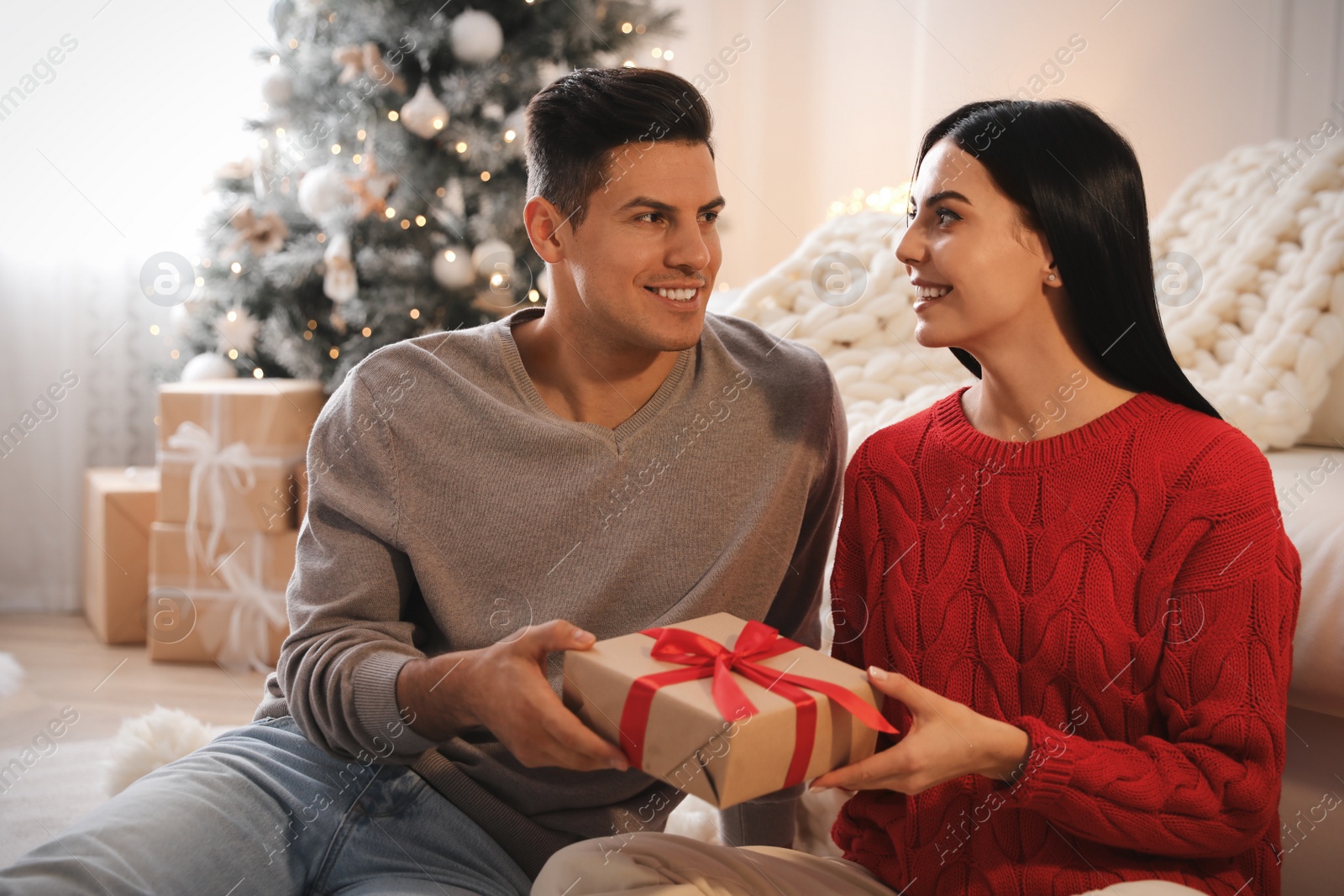 Photo of Couple holding gift box in room with Christmas tree