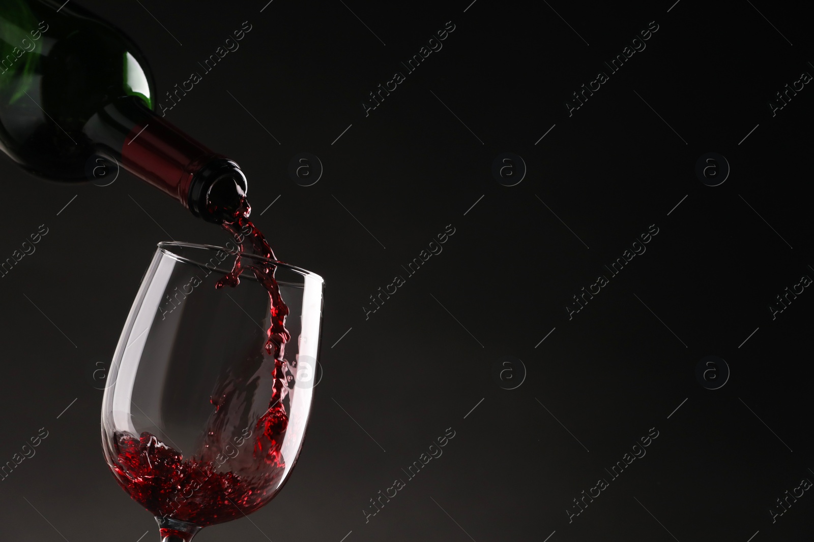 Photo of Pouring tasty red wine from bottle into glass on dark background, closeup. Space for text