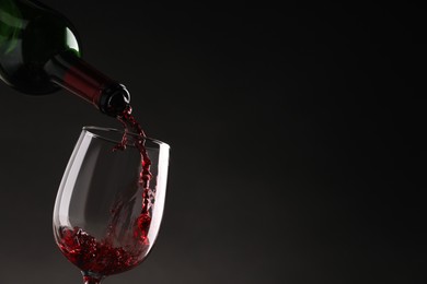 Photo of Pouring tasty red wine from bottle into glass on dark background, closeup. Space for text