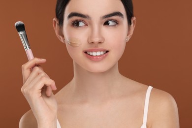 Photo of Teenage girl with swatch of foundation and makeup brush on brown background