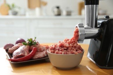 Photo of Modern meat grinder and products on wooden table in kitchen