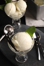 Tasty ice cream with vanilla pods in glass dessert bowls on dark grey table, above view