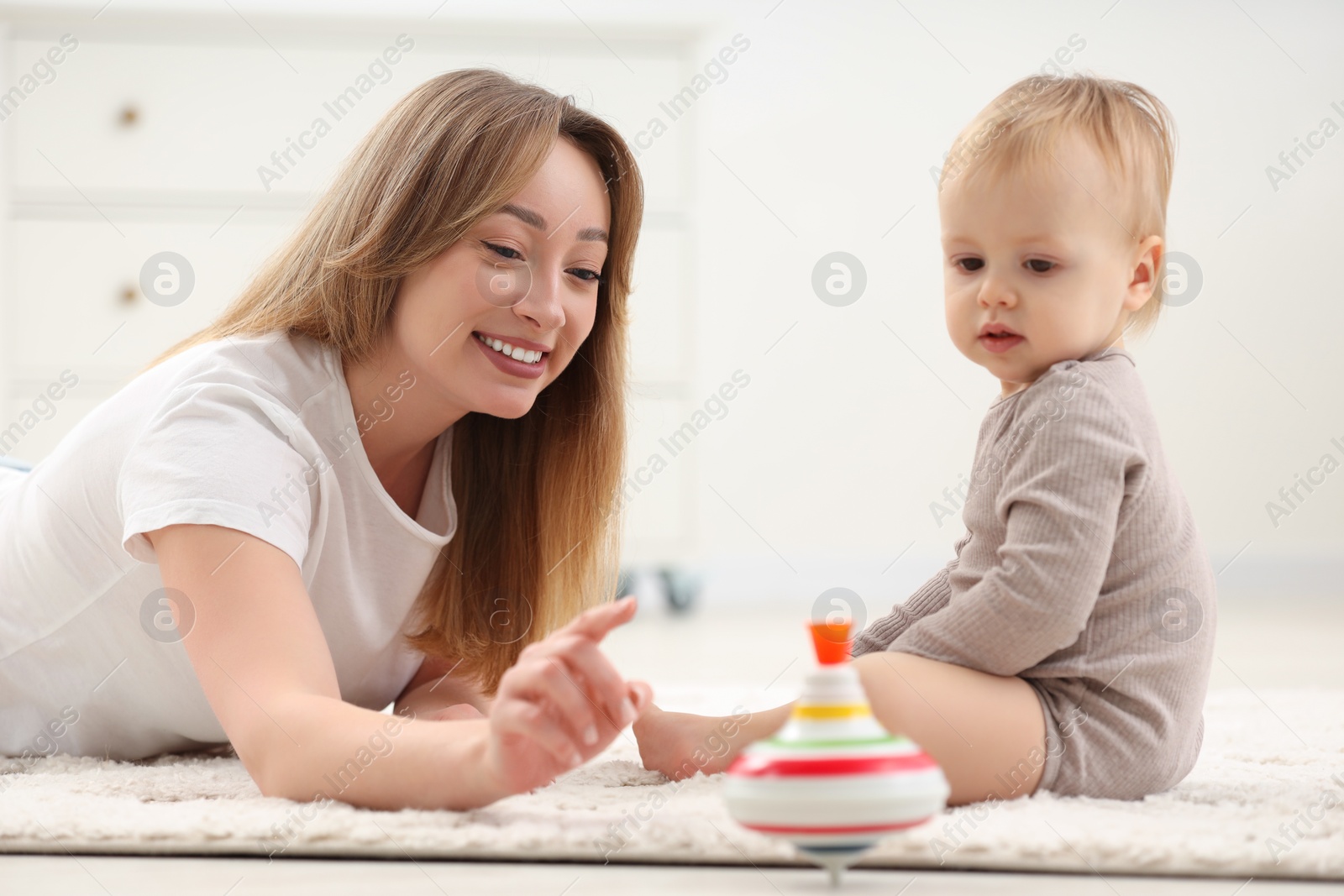 Photo of Children toys. Happy mother and her little son playing with spinning top on rug at home