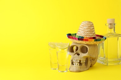 Human scull with Mexican sombrero hat, tequila and lime on yellow background, space for text