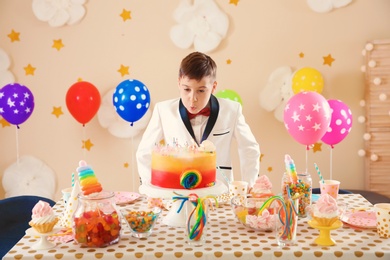 Cute little boy blowing out candles on his birthday cake indoors