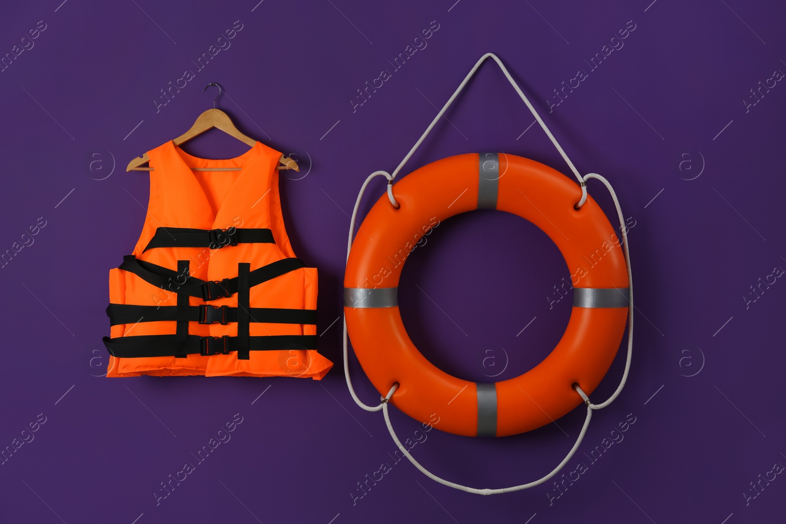 Photo of Orange life jacket and lifebuoy on violet background. Rescue equipment