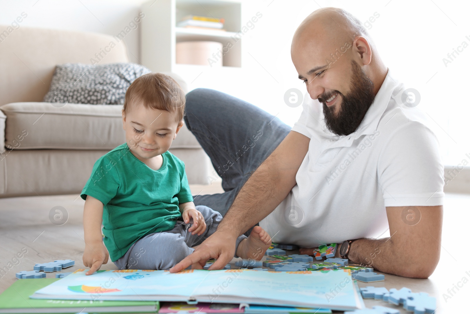 Photo of Dad and his little son reading book together at home