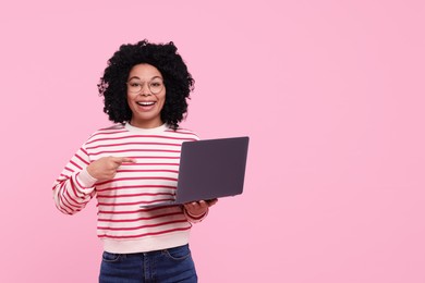 Photo of Happy young woman showing laptop on pink background. Space for text