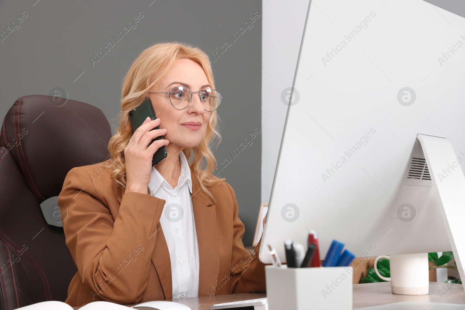 Photo of Lady boss talking on smartphone near computer at desk in office. Successful businesswoman