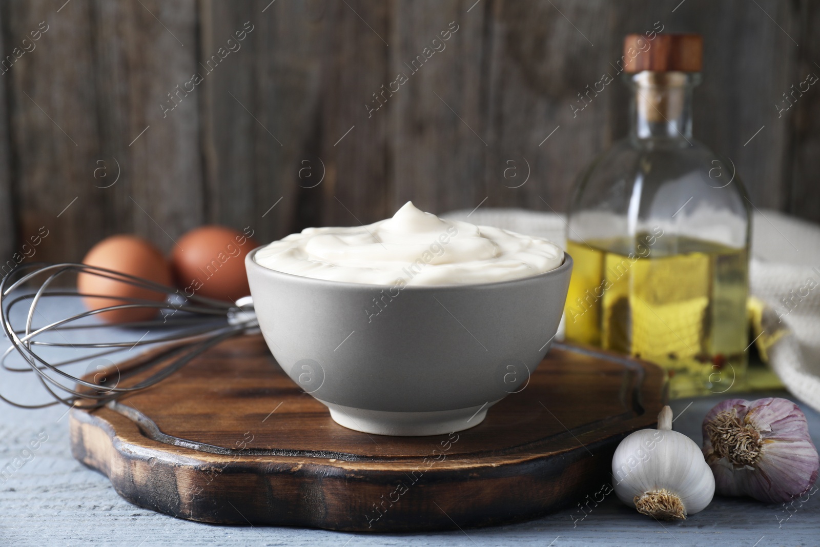 Photo of Tasty mayonnaise in bowl and ingredients on light grey wooden table, closeup