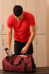 Photo of Handsome man taking bottle from sports bag in locker room